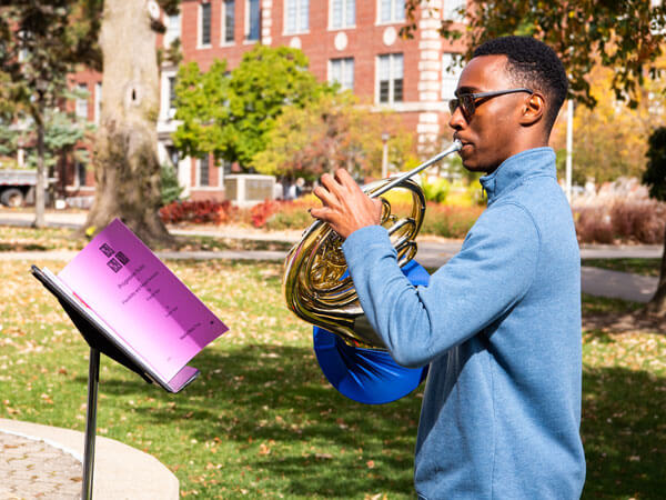 Student practices his french horn outside of Cook Hall.