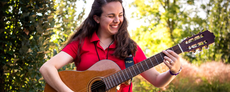 A music therapy student smiles while she plays the guitar.