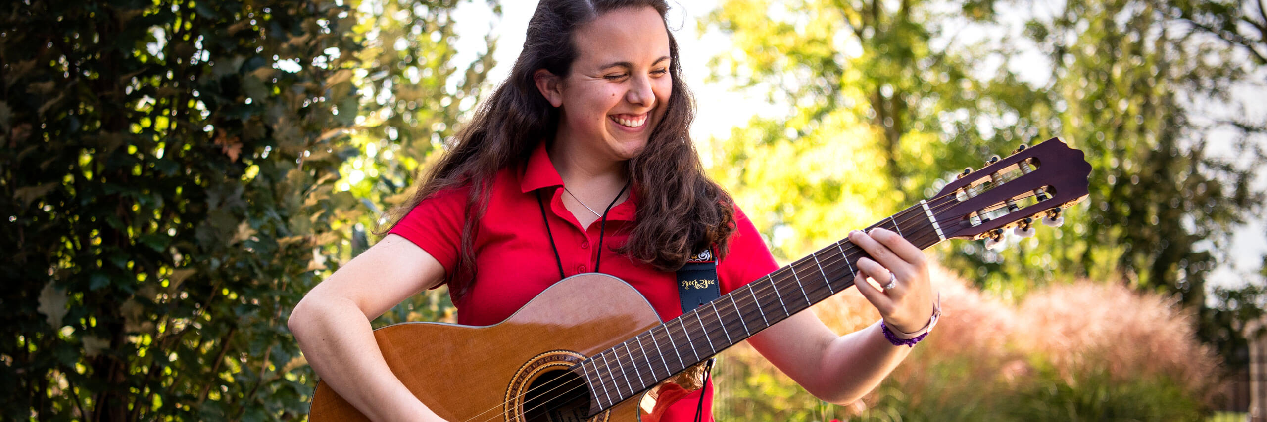 A music therapy student smiles while they play the guitar.