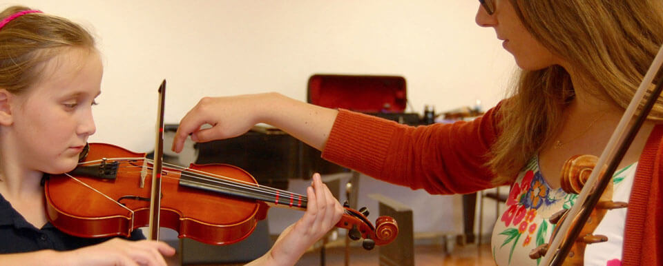 A student teacher gives a violin lesson to her student.
