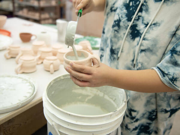 A student pour glaze into their ceramic mug.