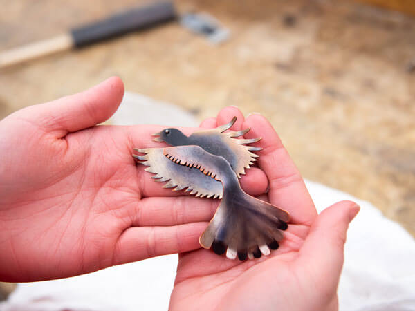 Student holds a small metal bird they made in a metals class.
