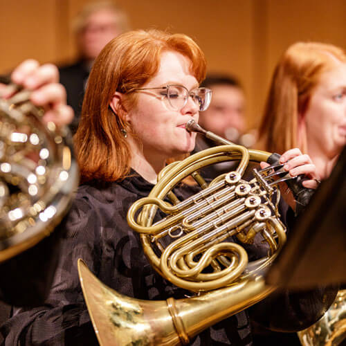 A member of the symphonic winds ensemble plays her french horn.
