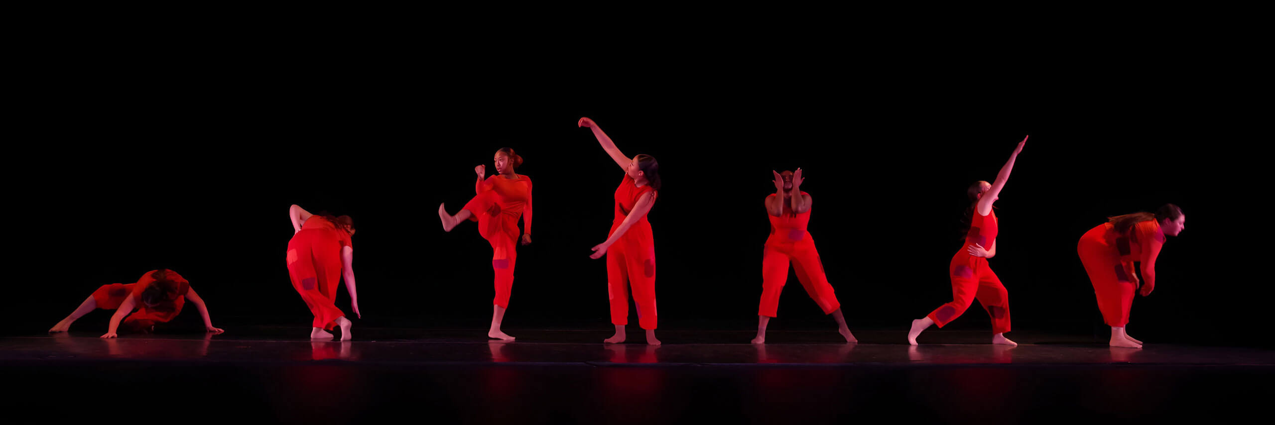 Dance students wearing red outfits hold dance poses on stage.