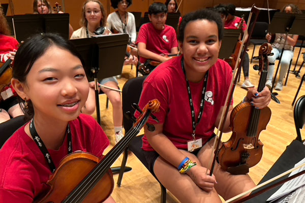 Two students in the string orchestra smile toward the camera.