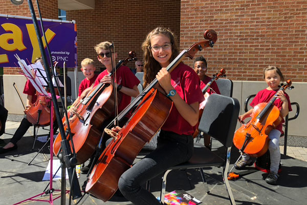 Students in a string orchestra smile for the camera.