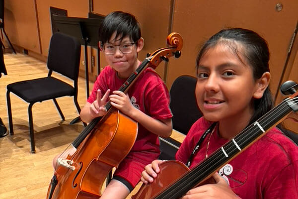 Two students in a string orchestra smile for the camera.