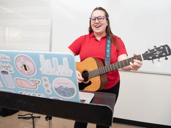 Music Therapy graduate students plays the guitar over a video call.