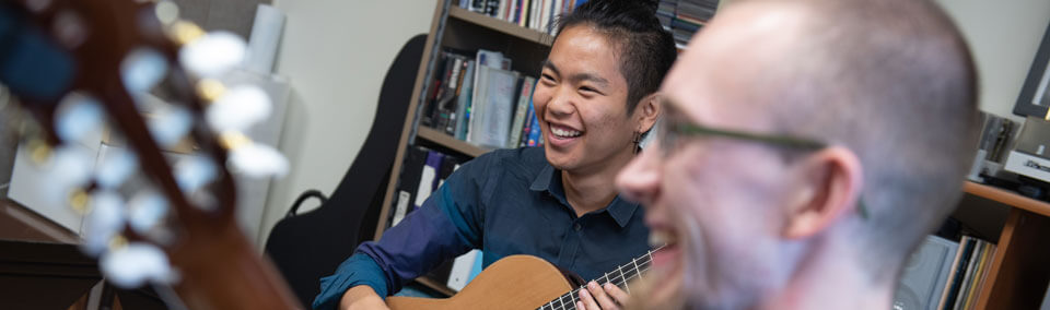 Two students in a guitar ensemble smile together.